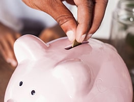 A hand putting a coin in a piggy bank